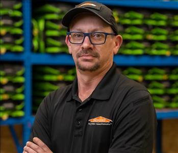 Chris is a white male wearing black glasses and a black servpro hat. He is wearing an all black servpro polo.