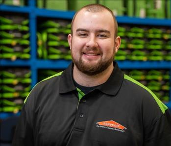 Alex is a white male who is bald and wearing a black and green servpro polo