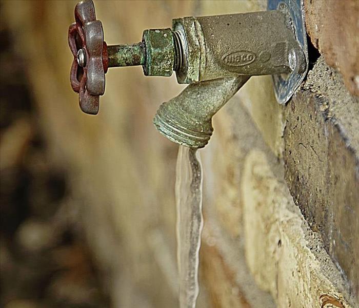 Bronze water faucet coming out of a brick wall with a frozen icicle