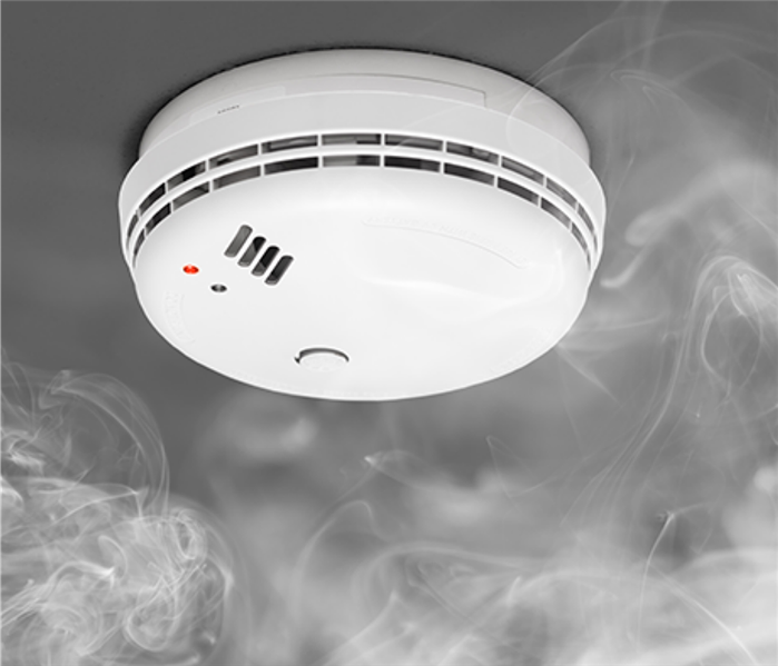 White smoke alarm on a grey ceiling with white smoke rising toward the smoke alarm
